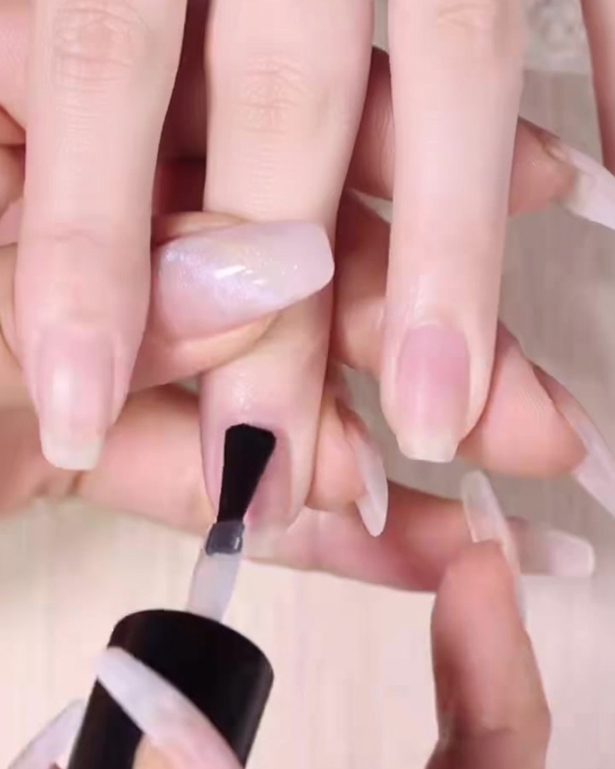 Un pinceau à ongles applique une couche lisse de base transparente sur un ongle naturel propre.
