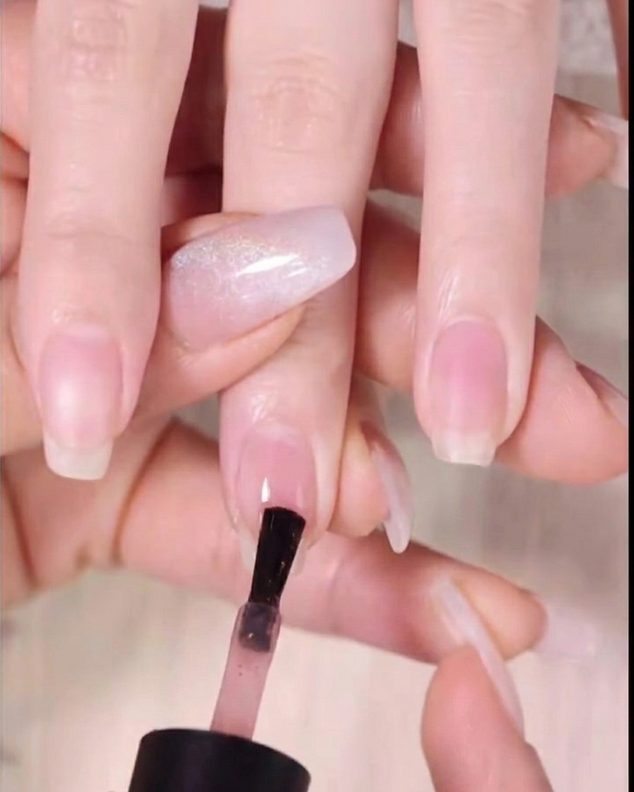 Un pinceau de vernis à ongles applique du gel ambre foncé sur le tiers supérieur de longle.