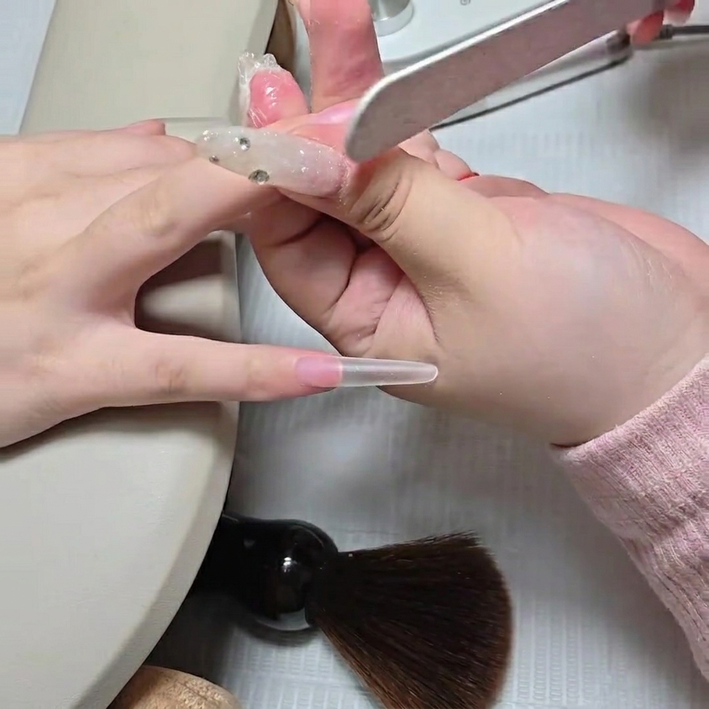 Une prothésiste utilisant une lime manuelle pour fondre la démarcation dune capsule stiletto transparente.