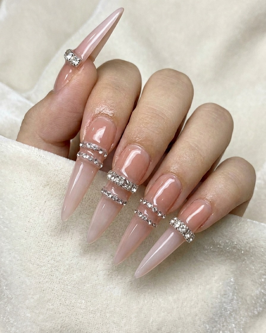 Un crayon à cire plaçant de petits strass transparents en ligne horizontale sur un ongle nude.