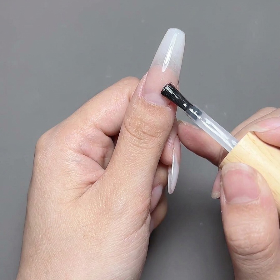 Un pinceau de top coat appliquant une couche de finition en gel transparent et brillant sur un design dongle terminé.