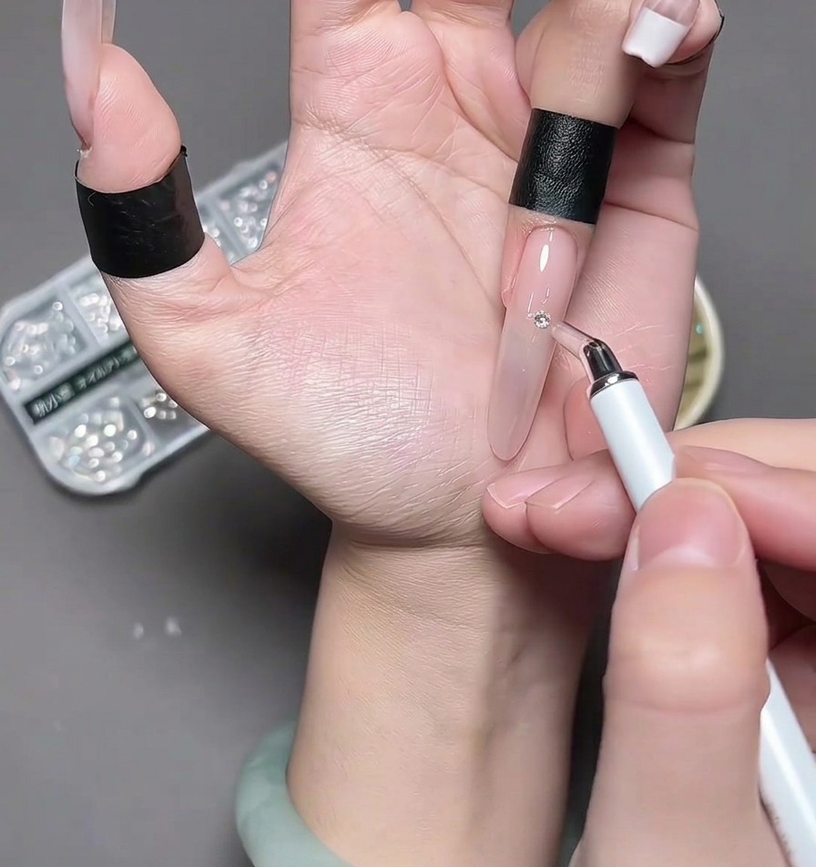 Des pincettes plaçant un petit bijou en forme de cœur en chrome argenté au centre dun ongle.