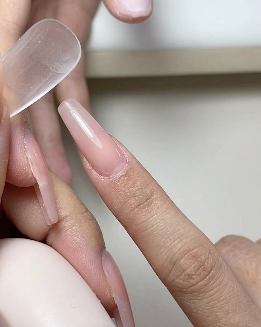 Un pinceau appliquant une fine couche transparente de base gel sur la surface dun ongle naturel.
