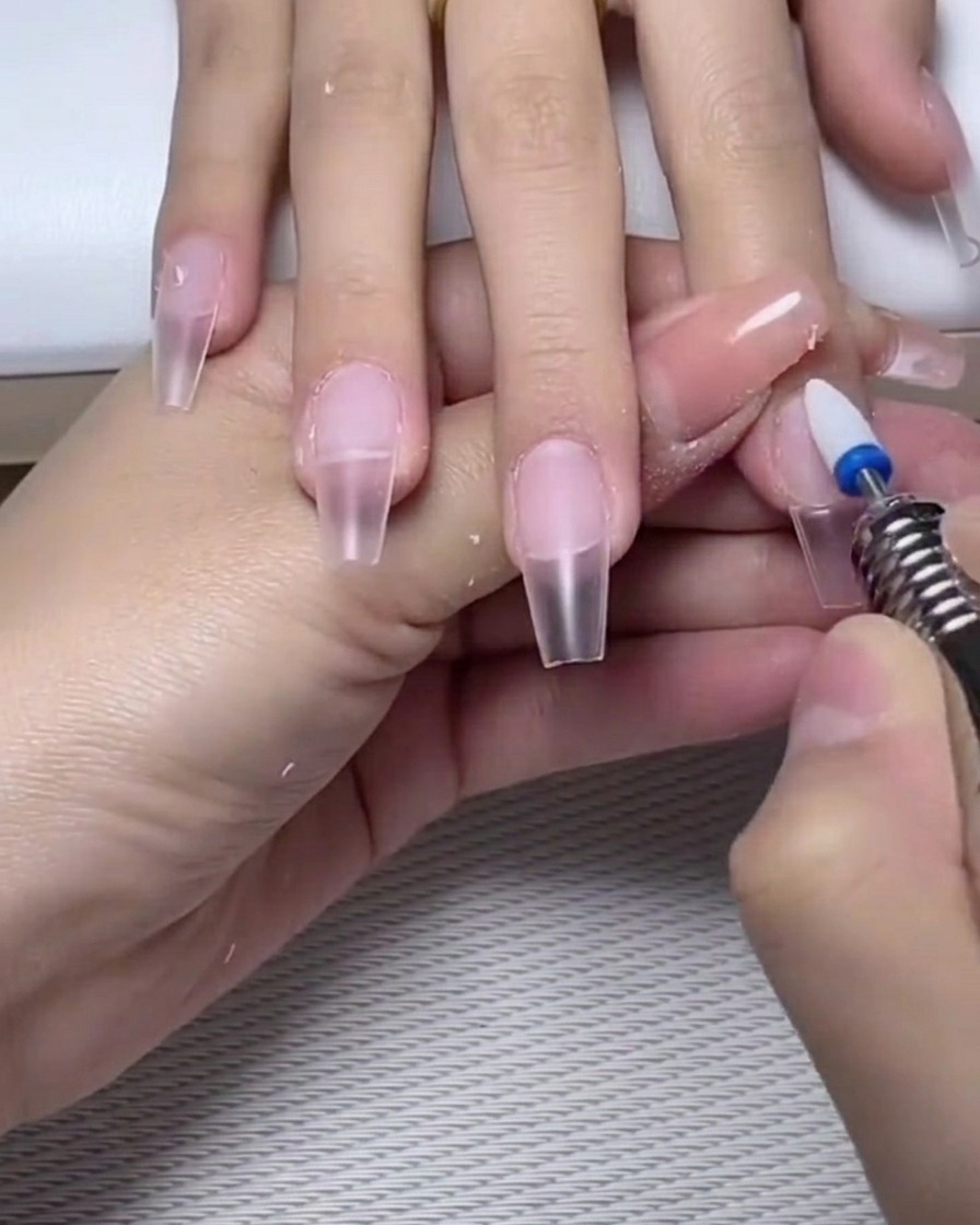 Une lime à ongles polissant légèrement la surface dune base gel catalysée sur longle.