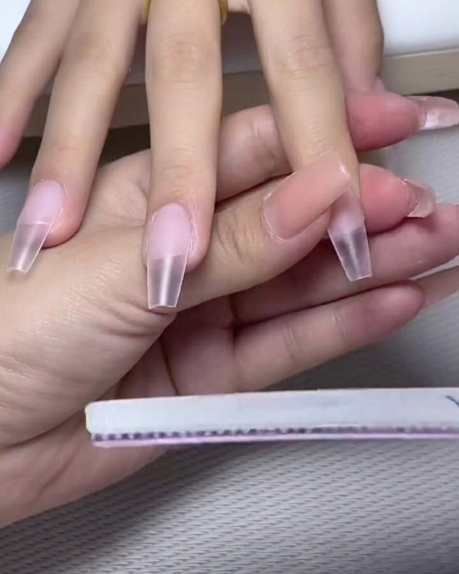 Un pinceau à ongles appliquant une couche de vernis gel blanc laiteux opaque sur la moitié supérieure de longle.