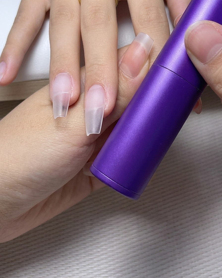 Une pince à épiler plaçant soigneusement un petit strass transparent sur un point de colle sur un ongle verni.