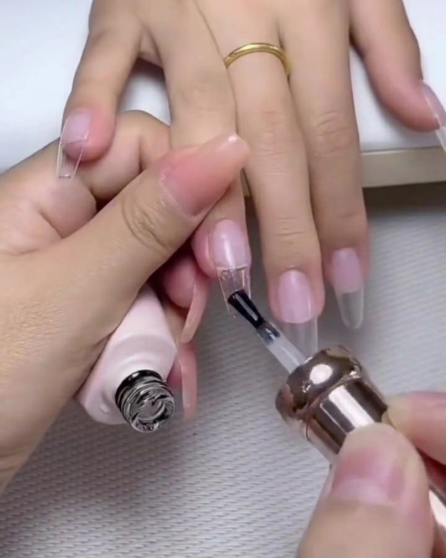 Un pinceau appliquant une couche de finition gel brillante sur un ongle décoré de perles et de strass.