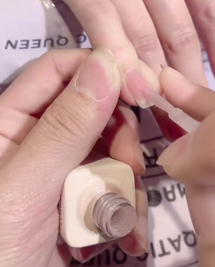 Un pinceau appliquant une fine couche lisse de gel de base nude diaphane sur un ongle.