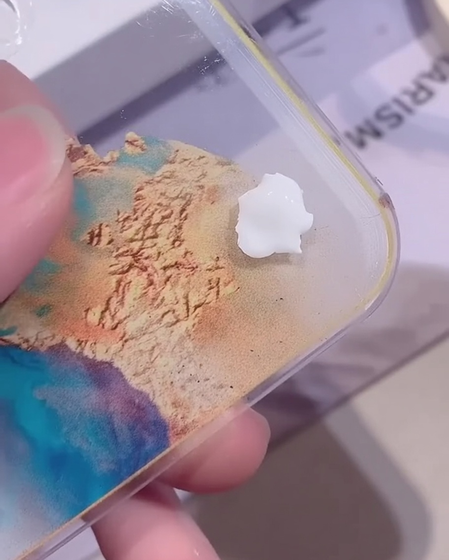 Une petite perle de gel de couleur blanc opaque reposant sur une palette de mélange acrylique transparente sur un fond coloré.