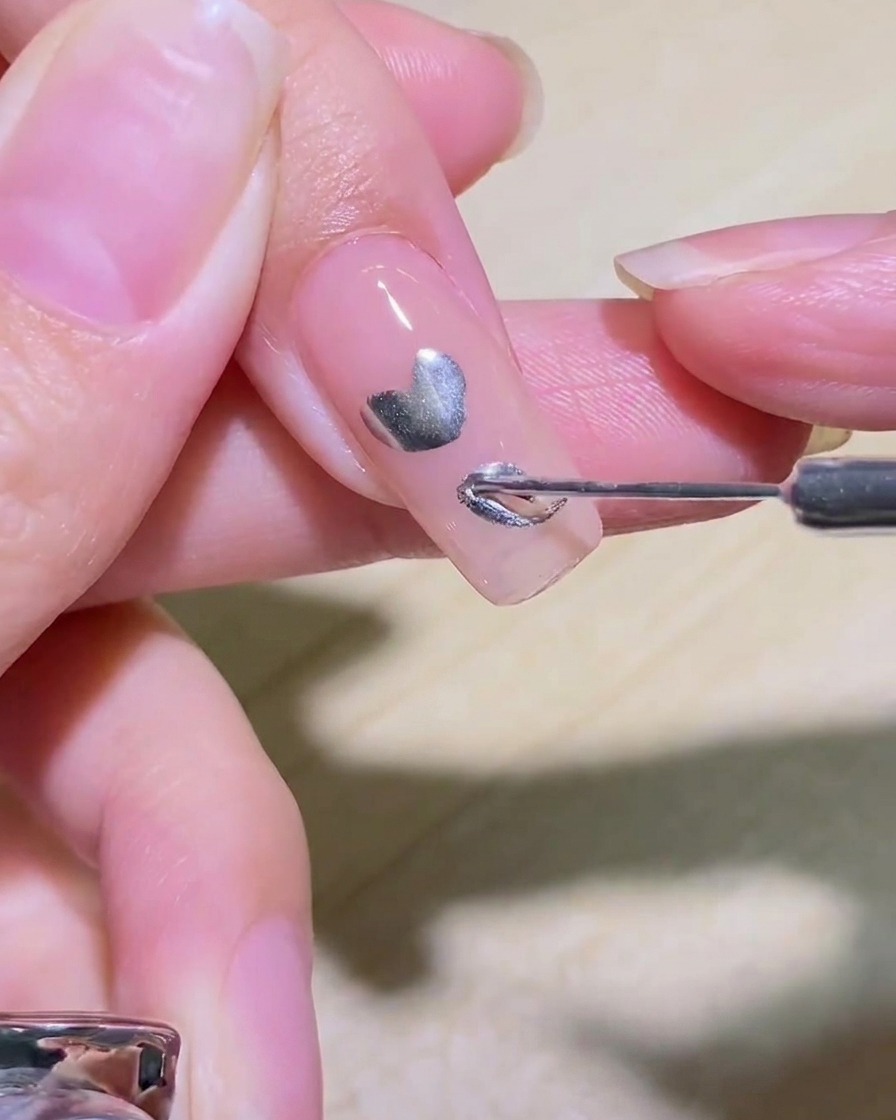 Un pinceau liner remplissant le centre dun cœur argenté sur un ongle.