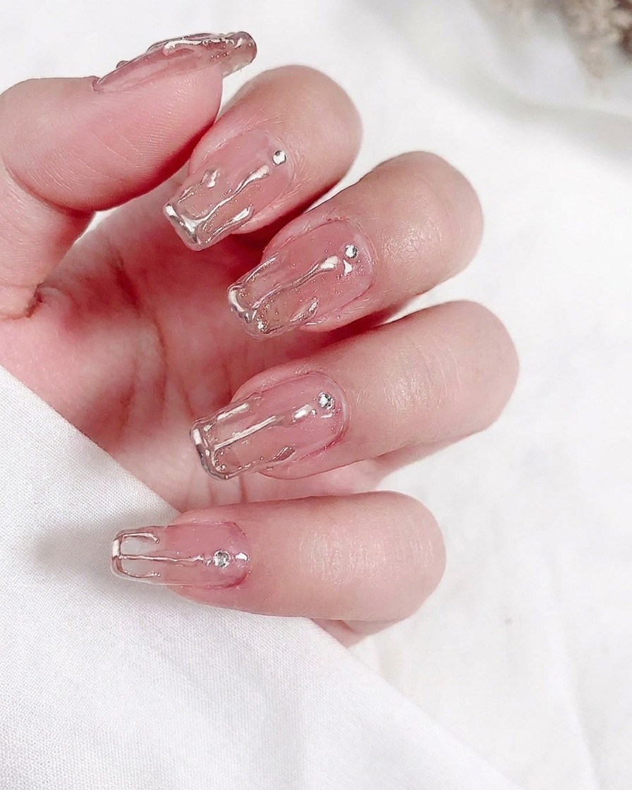 Gros plan dun pinceau appliquant une couche de vernis gel nude transparent sur un ongle naturel.