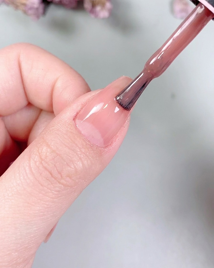 Un petit pinceau plat à gel lissant délicatement la couleur nude sur la surface de longle.
