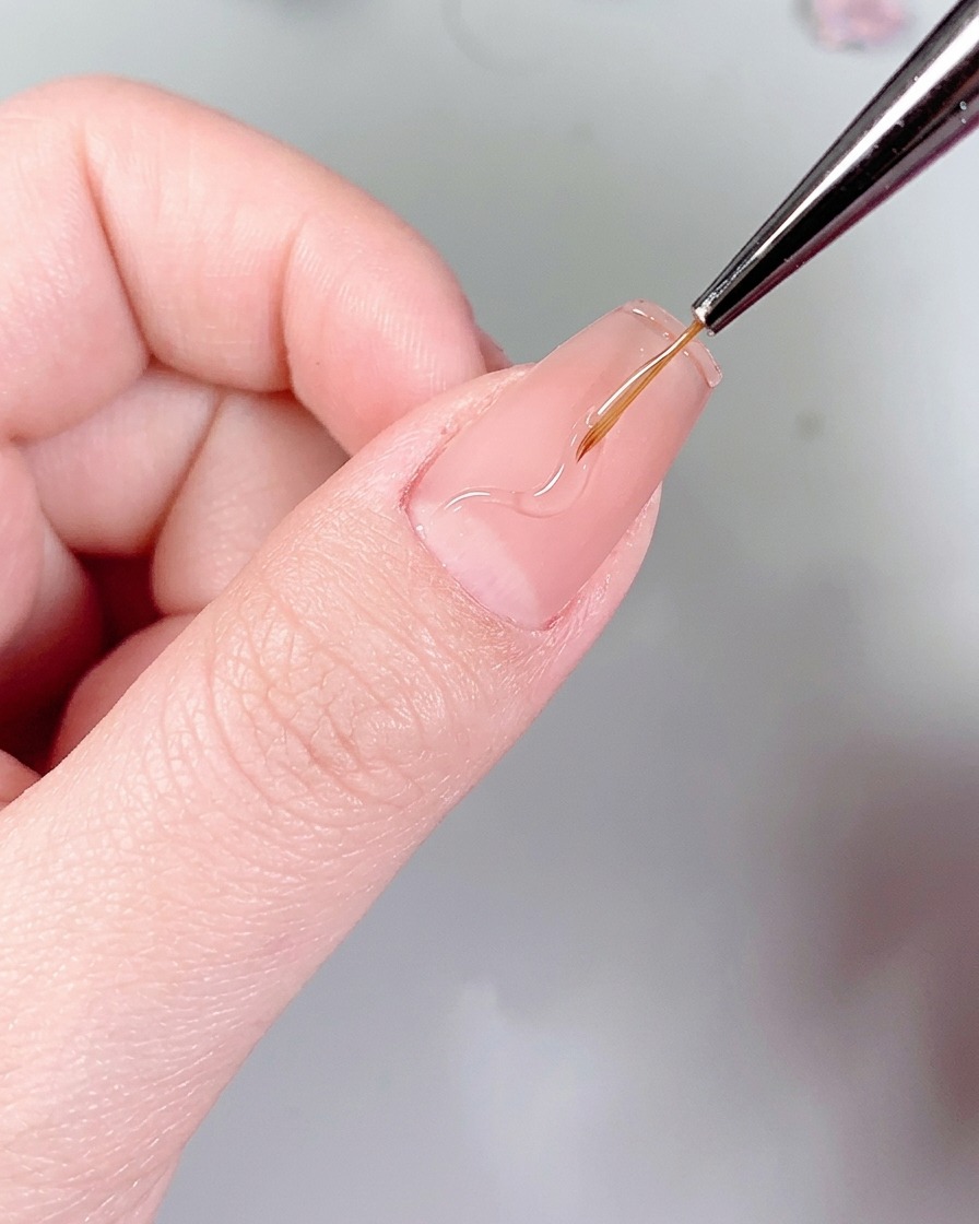 Un pinceau liner fin dessinant des motifs de flammes ondulées sur un ongle à laide de colle à ongles transparente.