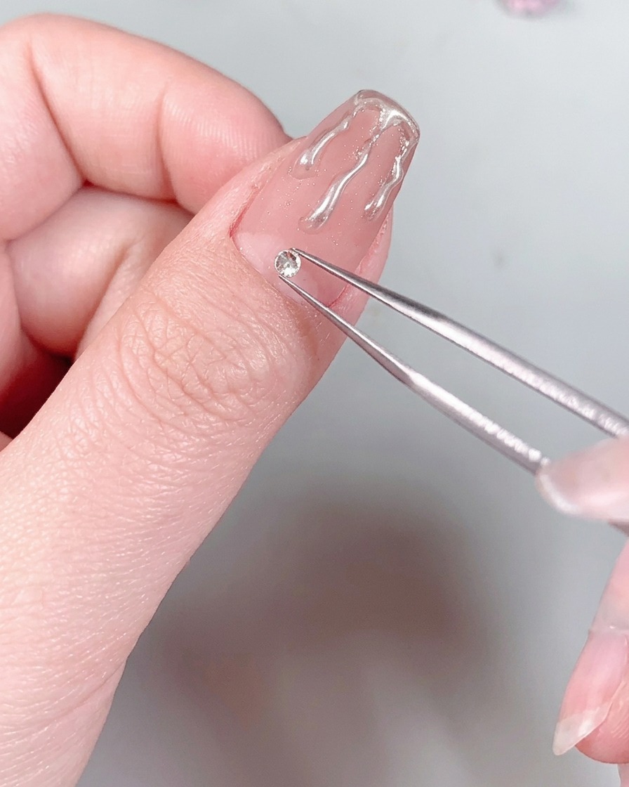 Un ongle manucuré avec un strass à la base placé sous la lumière dune lampe UV/LED.