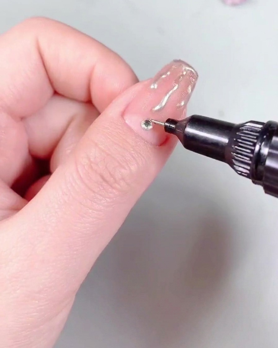 Un pinceau à nail art appliquant une couche de top coat brillant sur un ongle terminé.