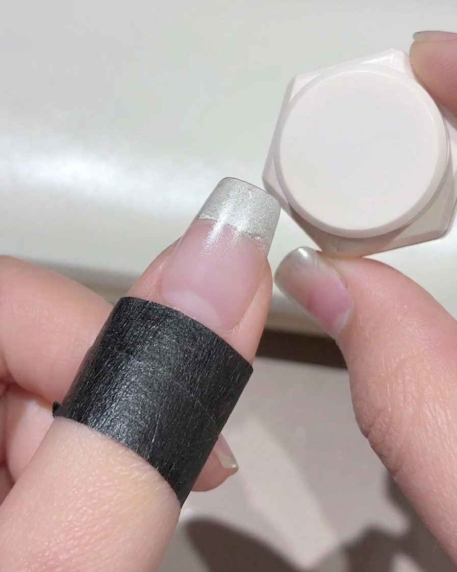Un gros plan dun doigt protégé par un ruban noir, montrant un gel blanc laiteux appliqué sur le bout de longle.