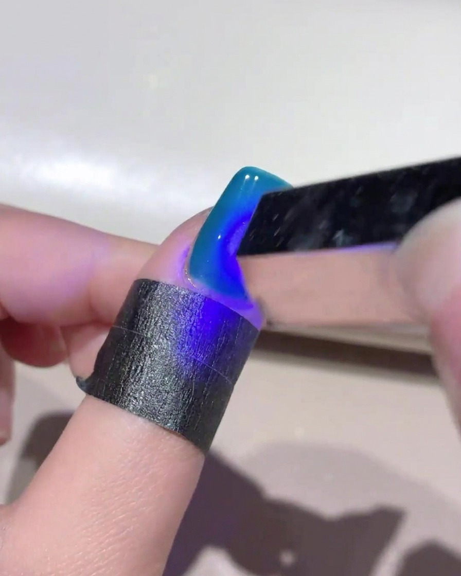 Une mini lampe UV portative projetant une lumière bleue sur un ongle en gel cat eye bleu profond pour fixer le design.