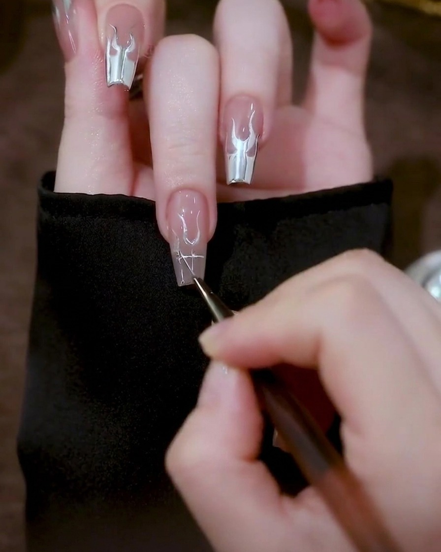 Gros plan dun ongle montrant des formes triangulaires en gel argenté dessinées de chaque côté des formes en U centrales.