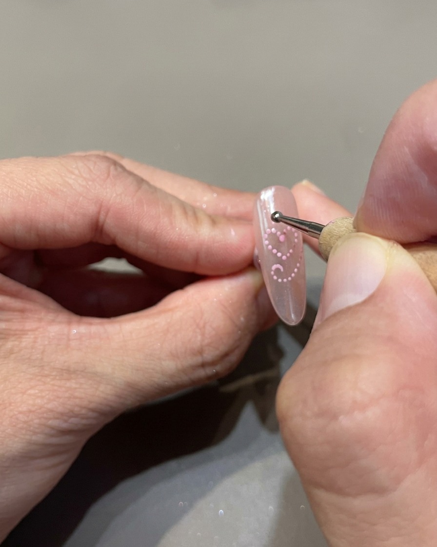 Un outil de dotting plaçant de petits points uniformes de gel cat-eye rose pour dessiner un cœur sur longle.