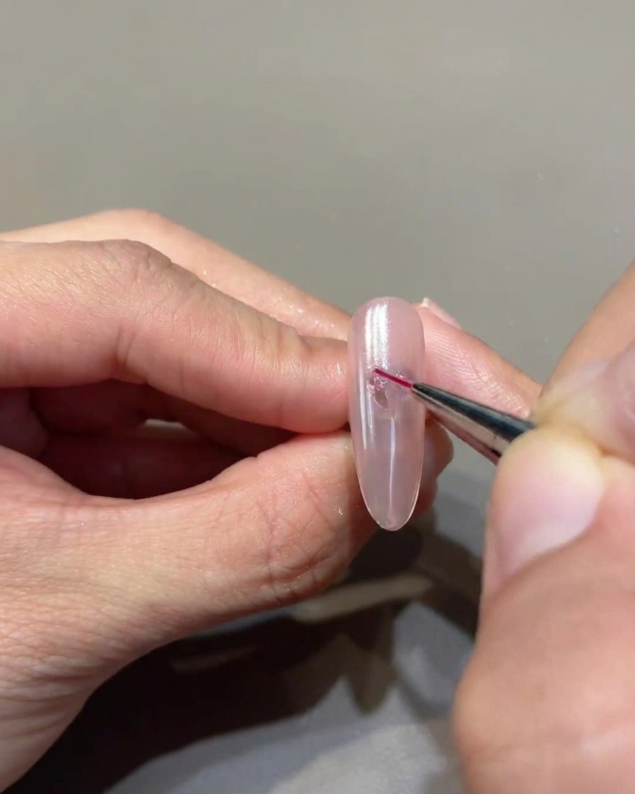 Un pinceau liner fin reliant méticuleusement les points de gel pour former un cœur net et précis sur longle.