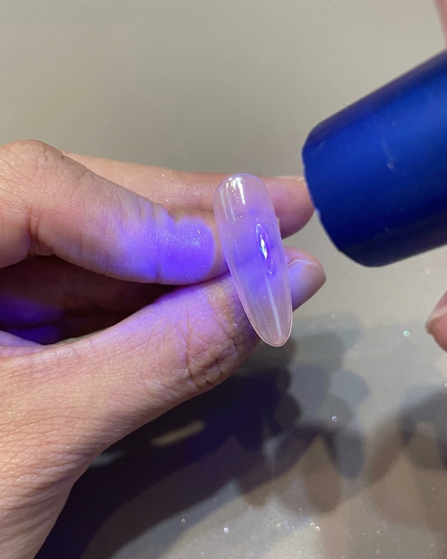 Un pinceau à vernis appliquant un top coat transparent brillant sur un ongle manucuré.