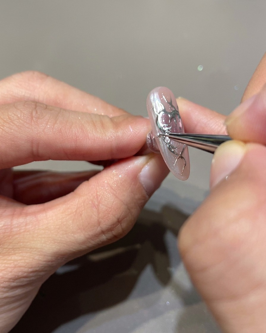 Gros plan sur un ongle décoré avec un pinceau fin appliquant du gel de construction 3D transparent sur les contours des flammes noires.