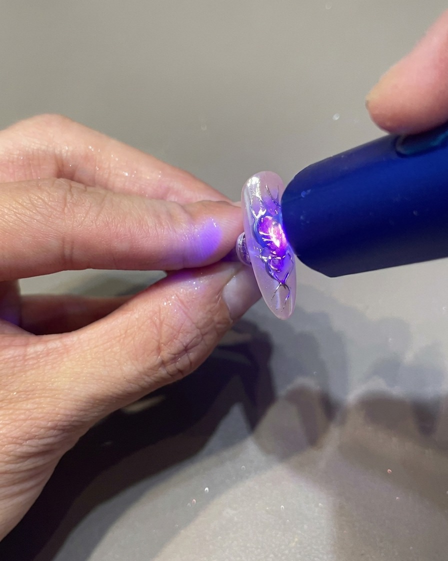Une lampe UV portable tenue au-dessus dun ongle pour fixer les détails en gel 3D transparent sur un design de cœur orné de flammes.