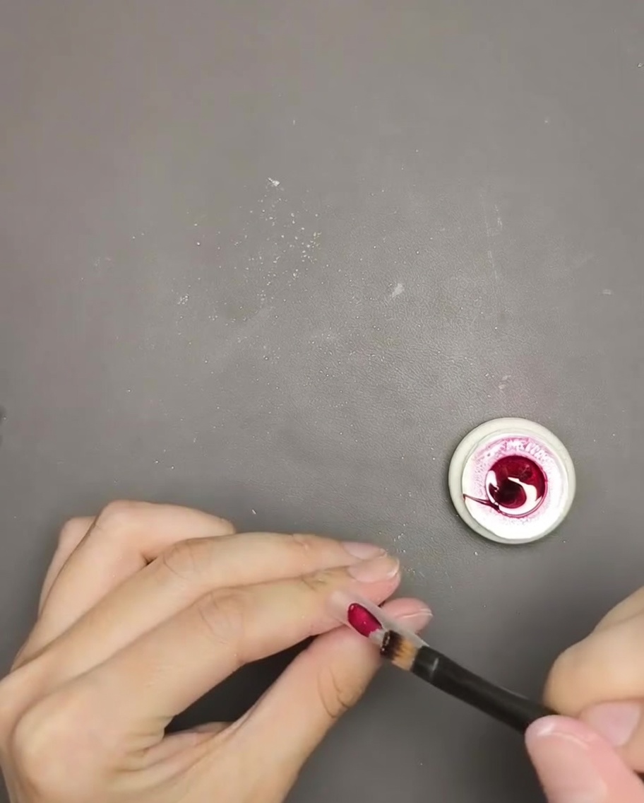 Gros plan sur un pinceau appliquant du gel œil de chat rouge profond sur une capsule dongle.