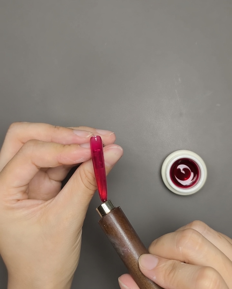 Une main utilisant un aimant près dun ongle en gel rouge pour révéler la ligne magnétique.