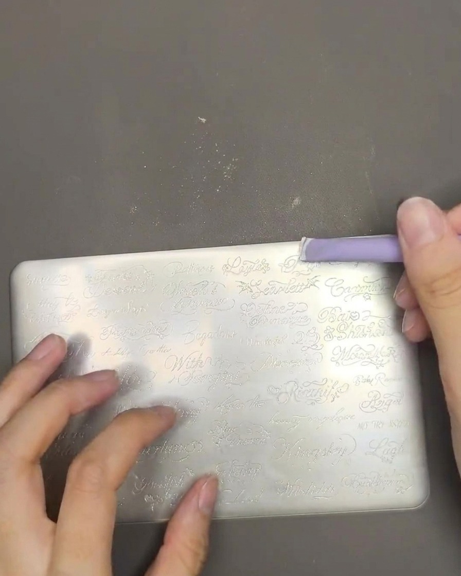 Gros plan montrant du vernis blanc étalé sur une plaque de stamping avec une raclette violette.
