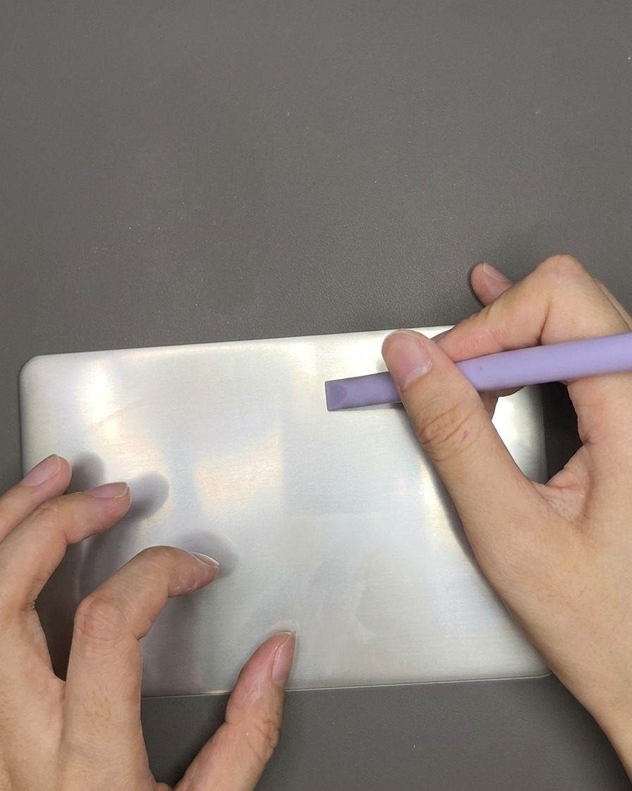 Un grattoir plastique passant sur une plaque de stamping pour enlever le vernis blanc en trop.