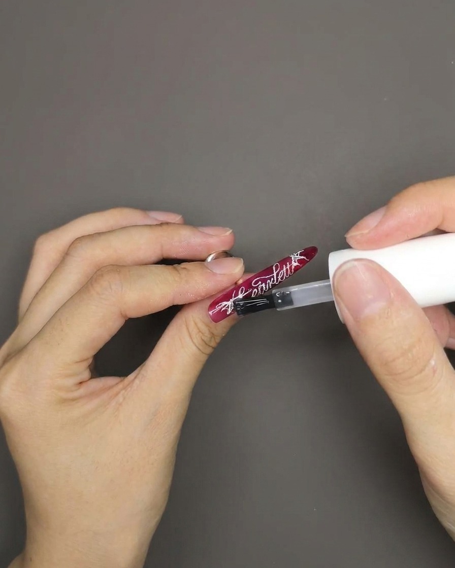 Un pinceau appliquant un top coat brillant sur un ongle rouge œil de chat avec texte blanc.