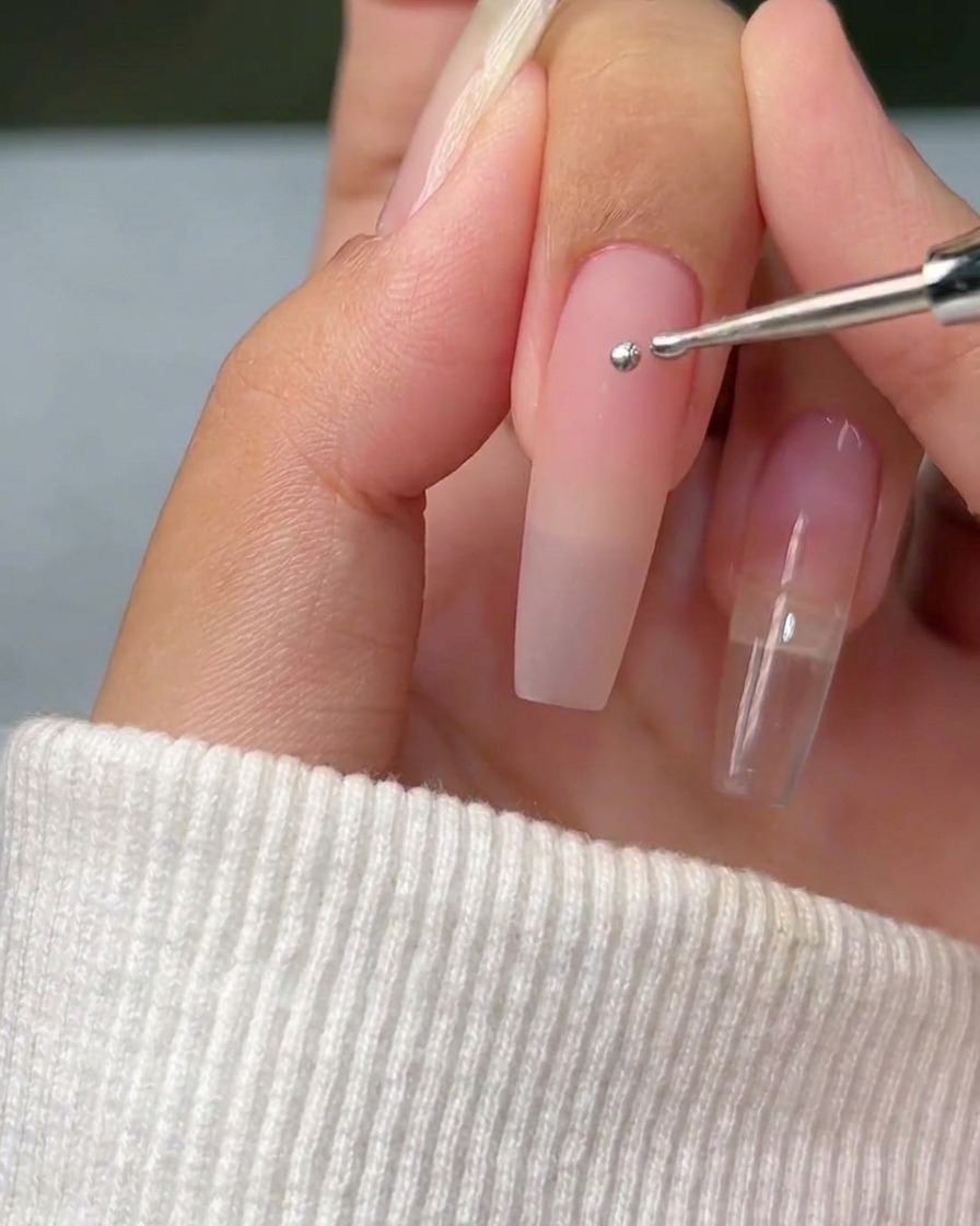 Gros plan dun outil de dotting déposant une sphère parfaite de gel métallique argenté sur une surface dongle naturel propre.