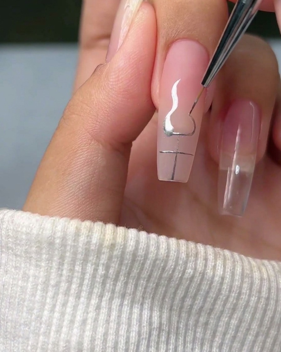 Un pinceau liner traçant des courbes élégantes en forme de flamme partant des coins dune croix argentée sur un ongle.
