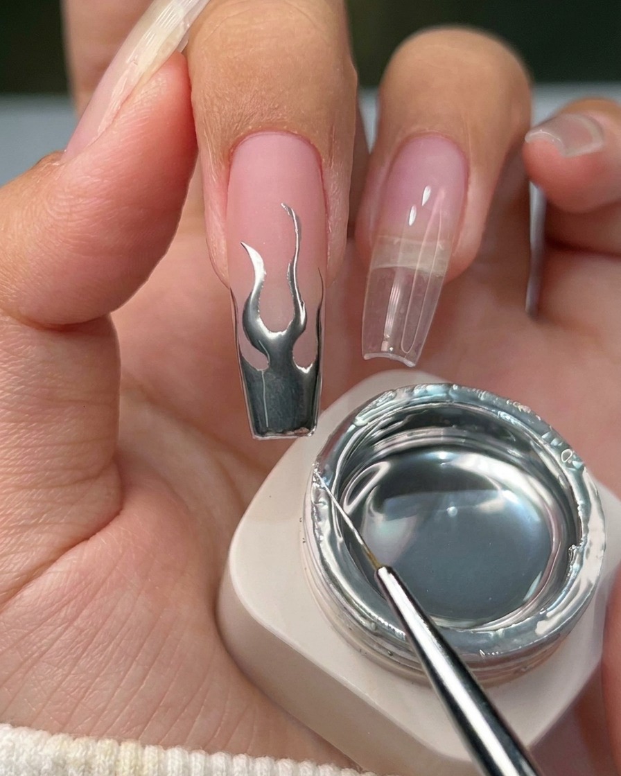Gros plan dun ongle fini avec un design de flamme argentée métallique sur une base neutre.
