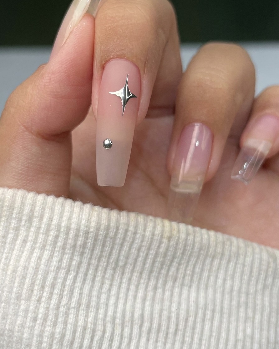 Un pinceau liner fin dessinant de fines lignes argentées en motif détoile sur un ongle.