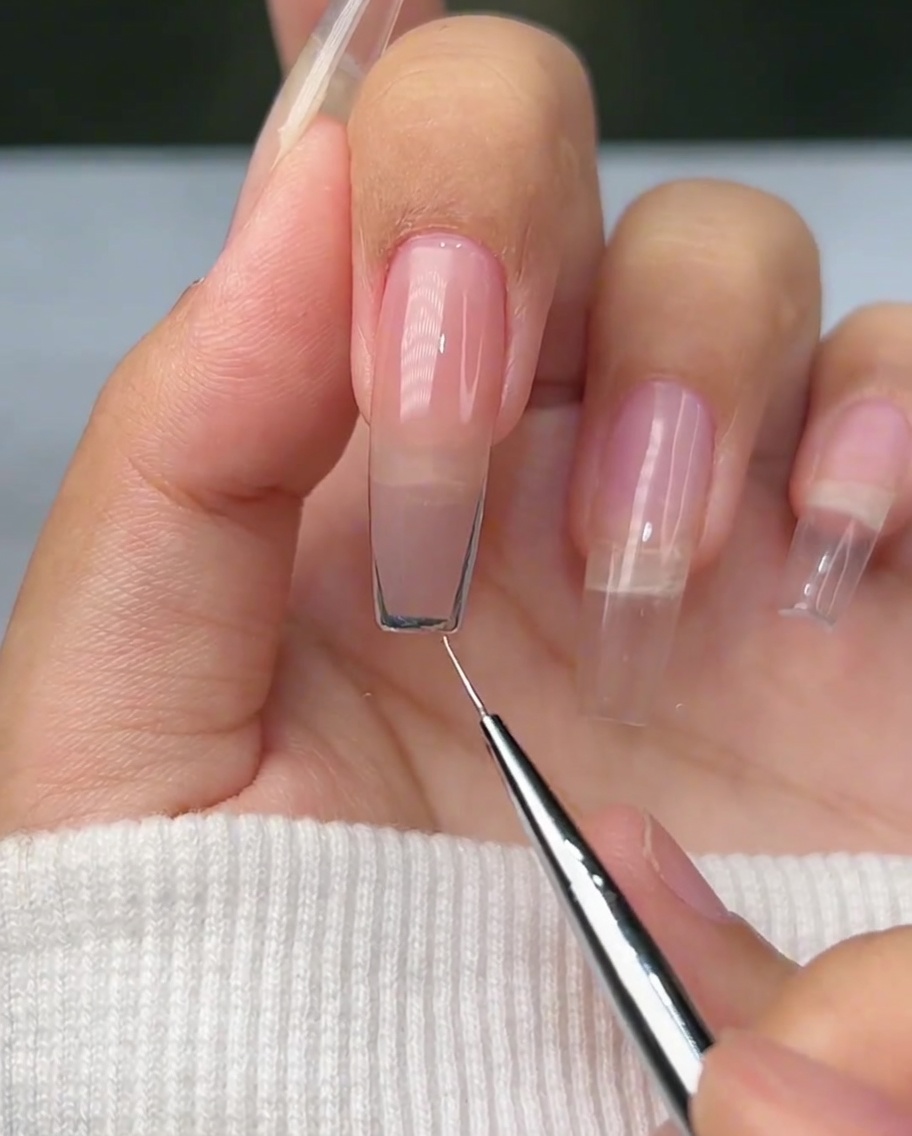 Gros plan dun pinceau liner créant un contour argenté incurvé sur le bord libre dun ongle naturel.