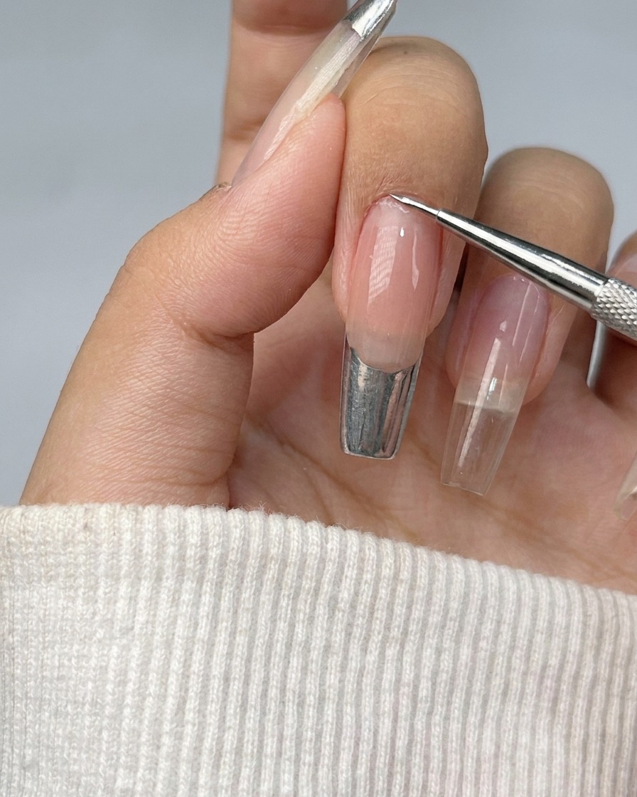 Un ongle avec une French manucure en cours de remplissage avec un gel métallique argenté brillant.