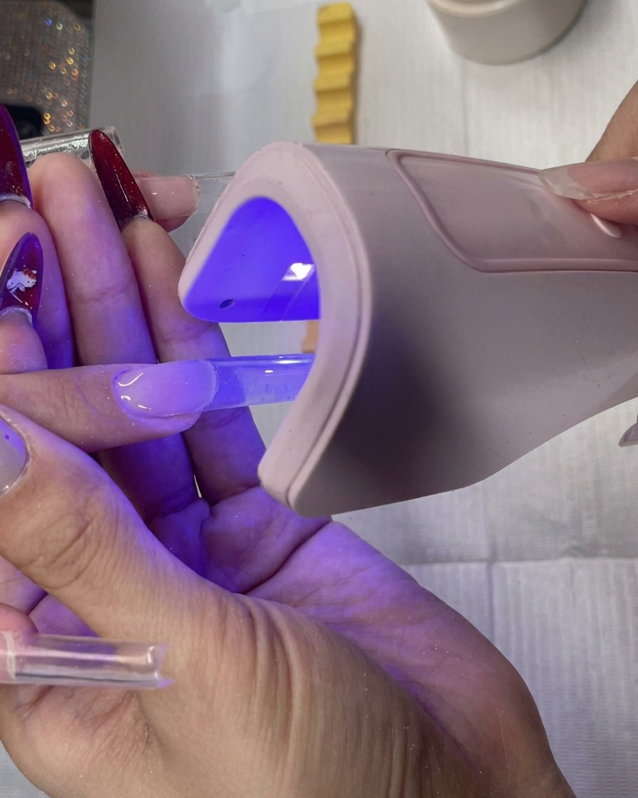 Une styliste ongulaire utilisant une petite lampe LED rose pour catalyser une extension.