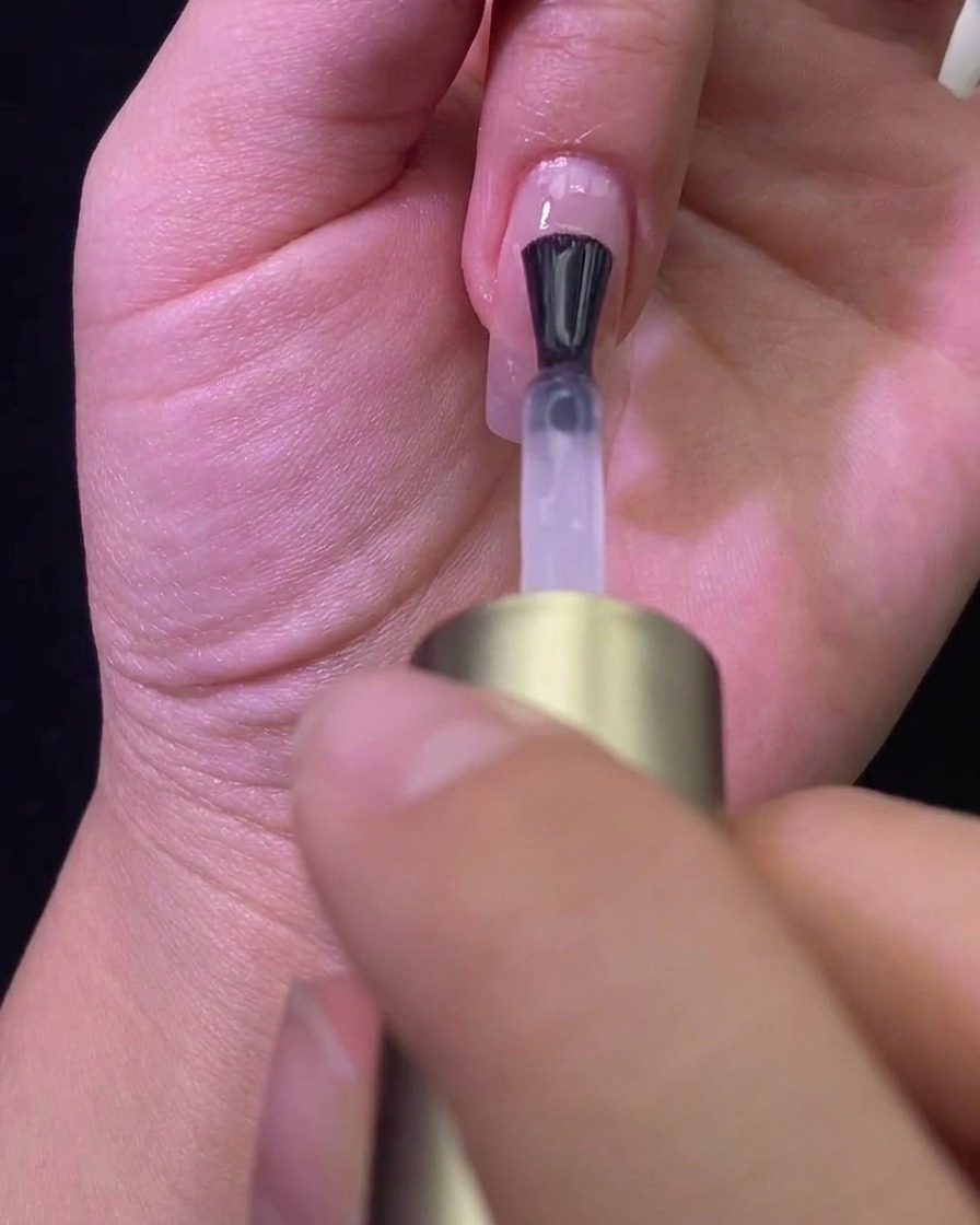 Un pinceau appliquant un top coat mat sur un ongle de couleur nude, transformant sa finition.