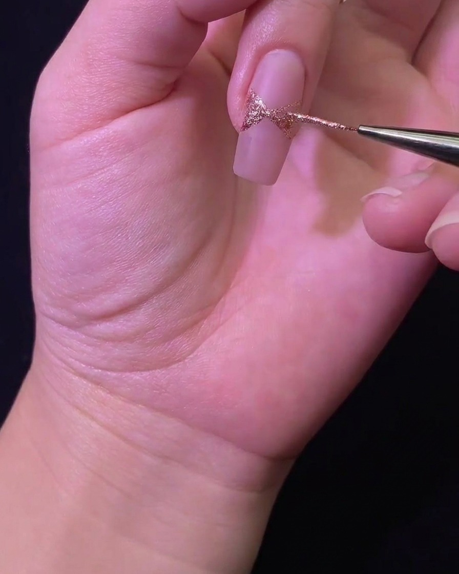 Gros plan dun pinceau liner remplissant la forme du nœud pailleté sur la surface de longle.