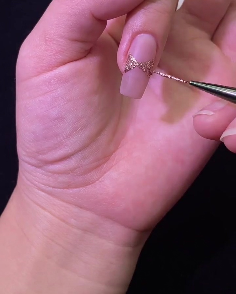 Un ongle positionné sous une lampe UV/LED pour catalyser le nail art du nœud en paillettes or rose.