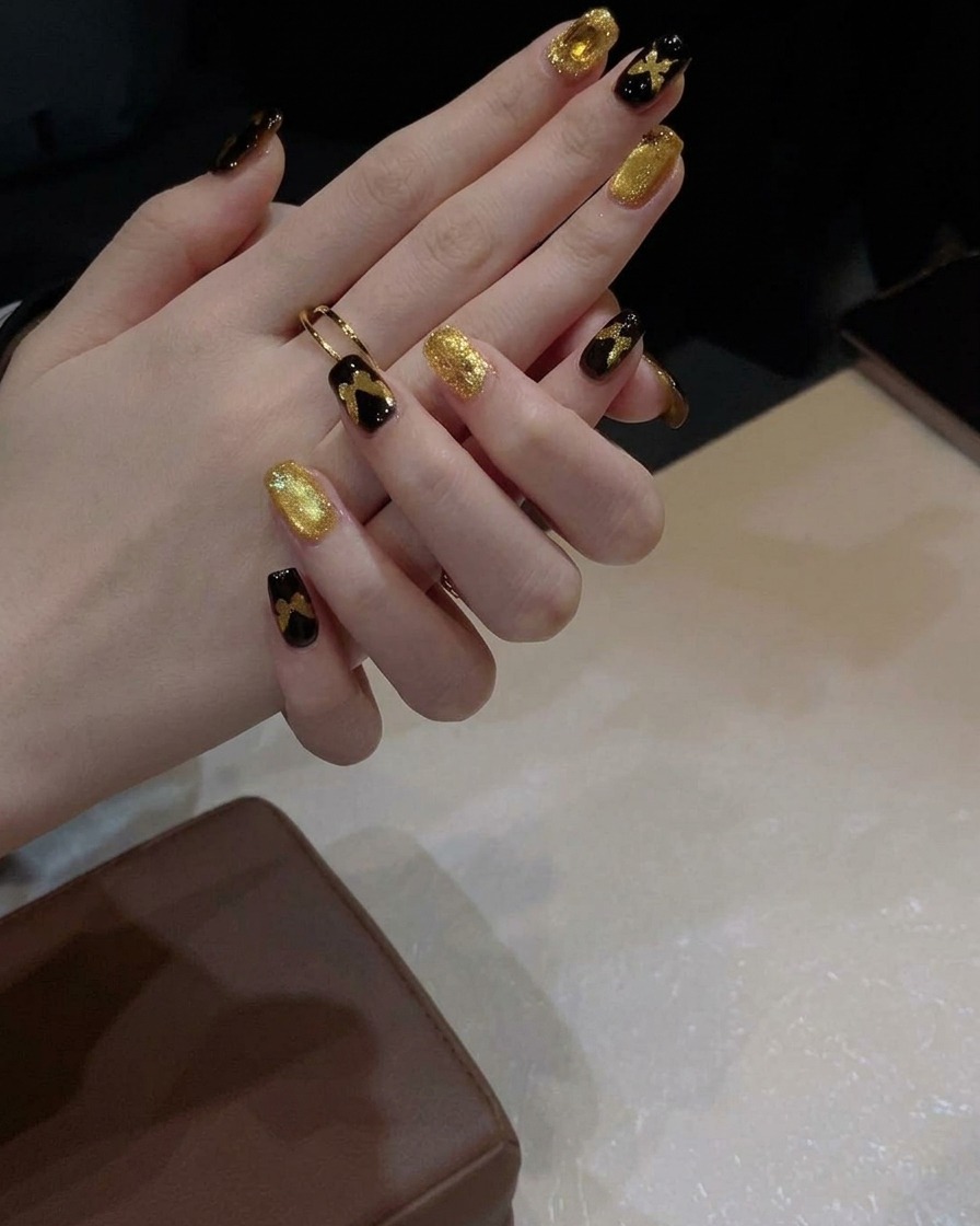 Un pinceau à gel appliquant une couche de vernis œil-de-chat doré scintillant sur un ongle peint en noir.