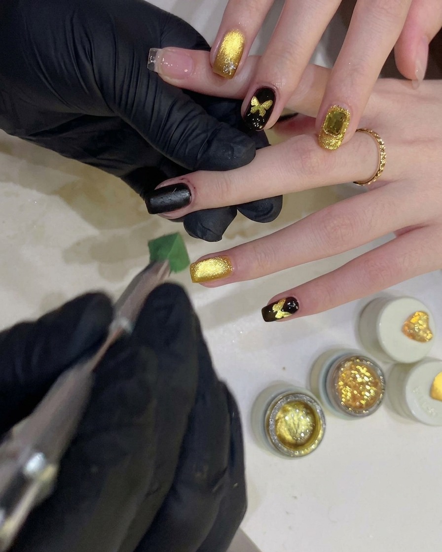 Une personne utilisant une éponge pour tamponner du gel noir sur un pochoir en forme de papillon sur un ongle.