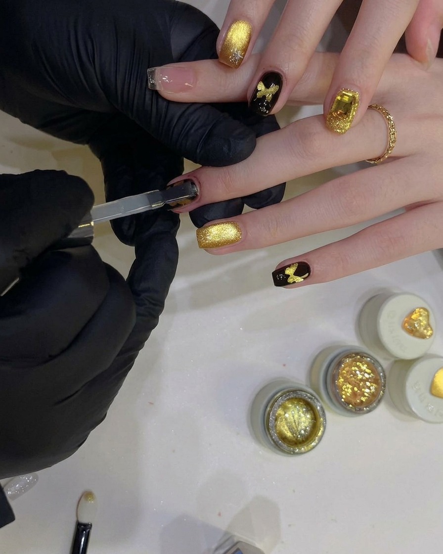 Un pinceau à gel plat appliquant un top coat transparent brillant sur un ongle noir avec un design de papillon doré étincelant.