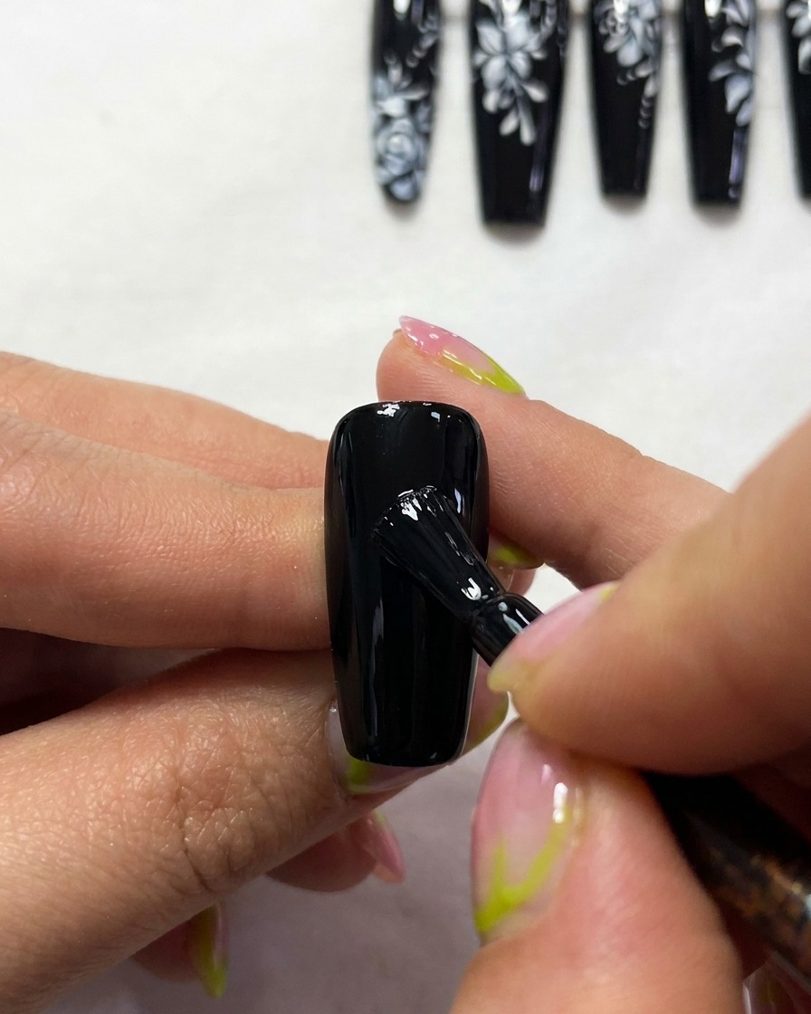 Gros plan dun pinceau peignant les contours blancs fins et élégants de la structure des ailes dun papillon sur un ongle noir.