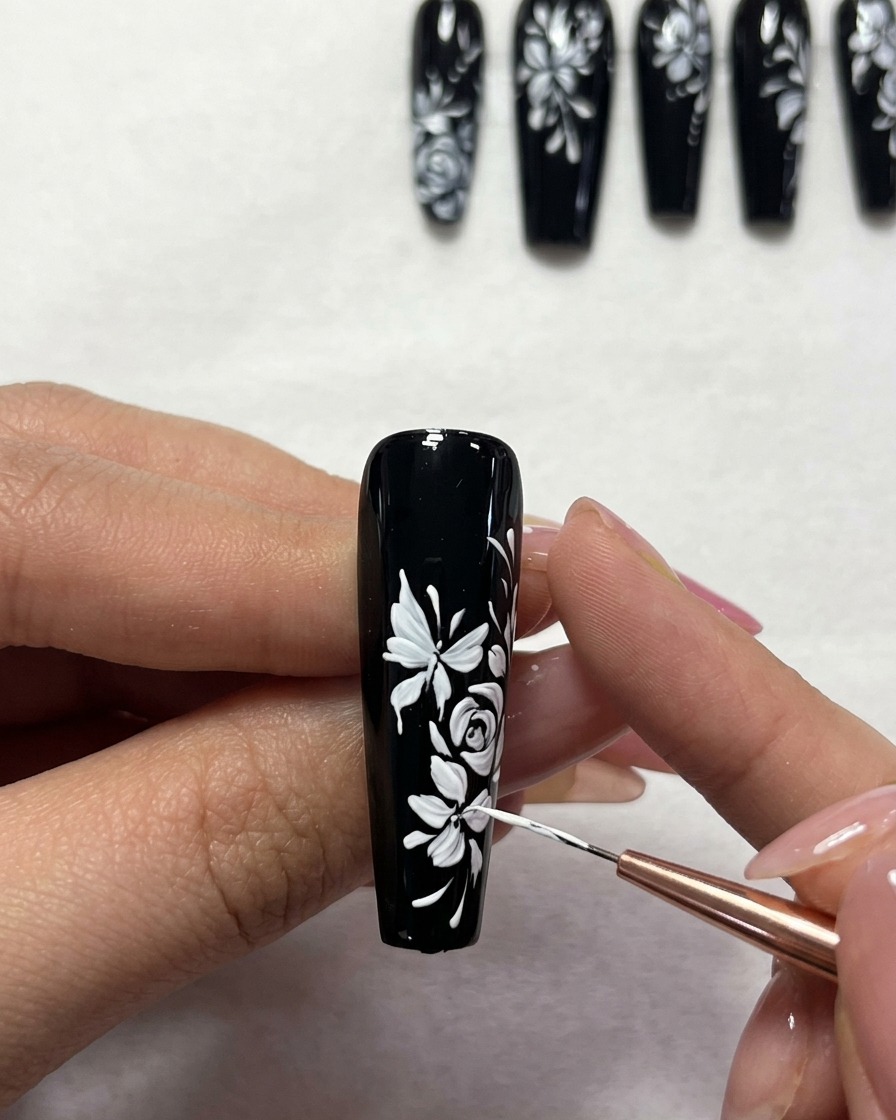 Gros plan dun pinceau de précision ajoutant de petits points blancs à un design dongle floral sur base noire.