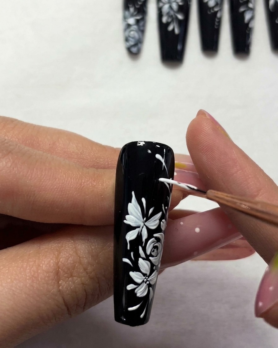 Un pinceau appliquant une couche de finition transparente sur le nail art floral fini.