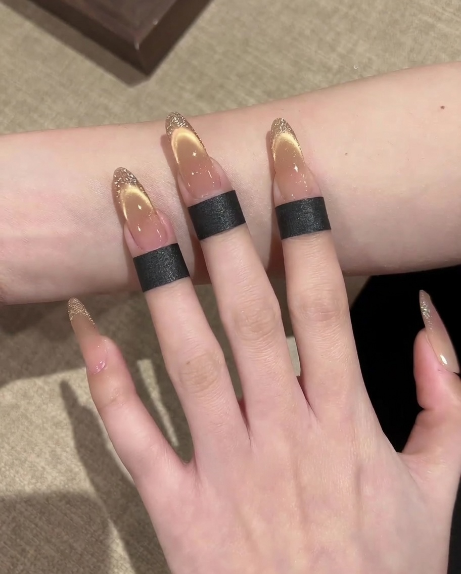 Gros plan sur une main utilisant un pinceau liner fin pour tracer un contour doré sur une French cat-eye.