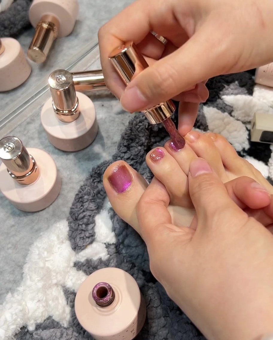 Un pinceau appliquant du gel rose sur un orteil, suivi dun aimant créant leffet cat-eye sur la surface humide.